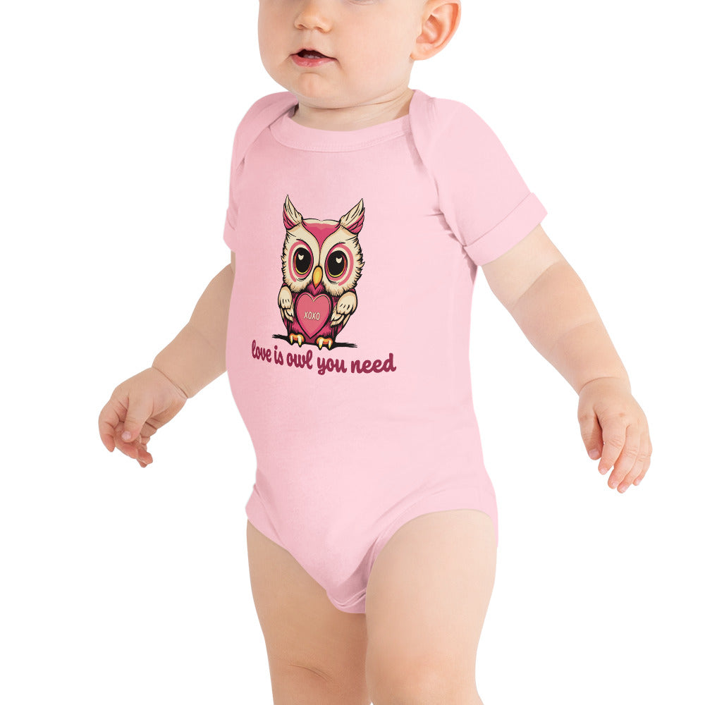 Pictured is a baby girl wearing a pink one piece bodysuit with short sleeves and 3 snaps. The adorable design on this baby clothing is       to be worn for Valentine's Day. The cute graphic design is a pink and beige colored owl holding a heart that says "xoxo". The words       underneath the owl artwork say "love is owl you need". This unique snapsuit infant clothing comes in 4 colors, pink, grey, yellow, and white.      Sizes available are 3-6 months, 6-12 months, and 12-18 months.